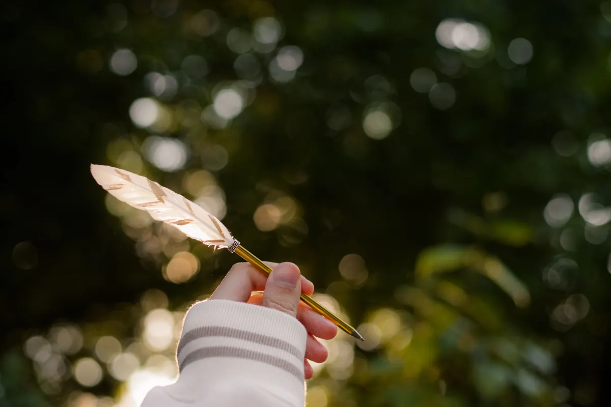 A hand holding a feather quill against soft green light